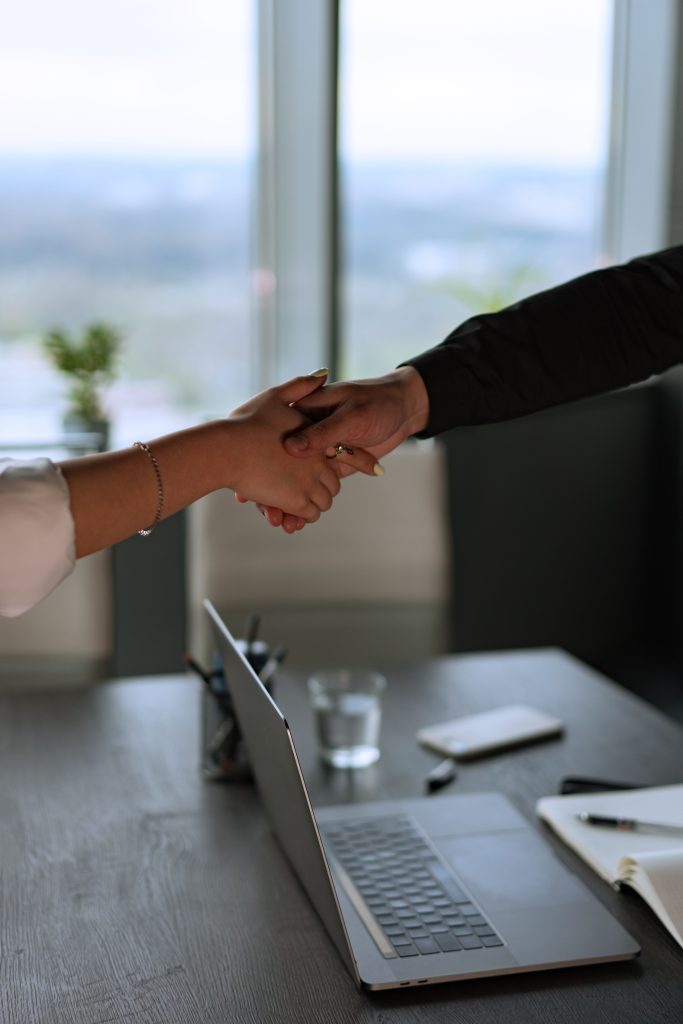 Home Business professionals shaking hands across a desk in a contemporary office with a laptop.